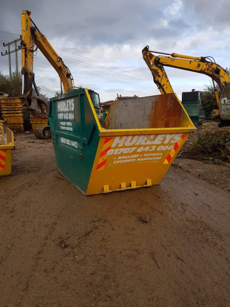 A green and yellow skip with Hurleys Skip Hire branding on it.