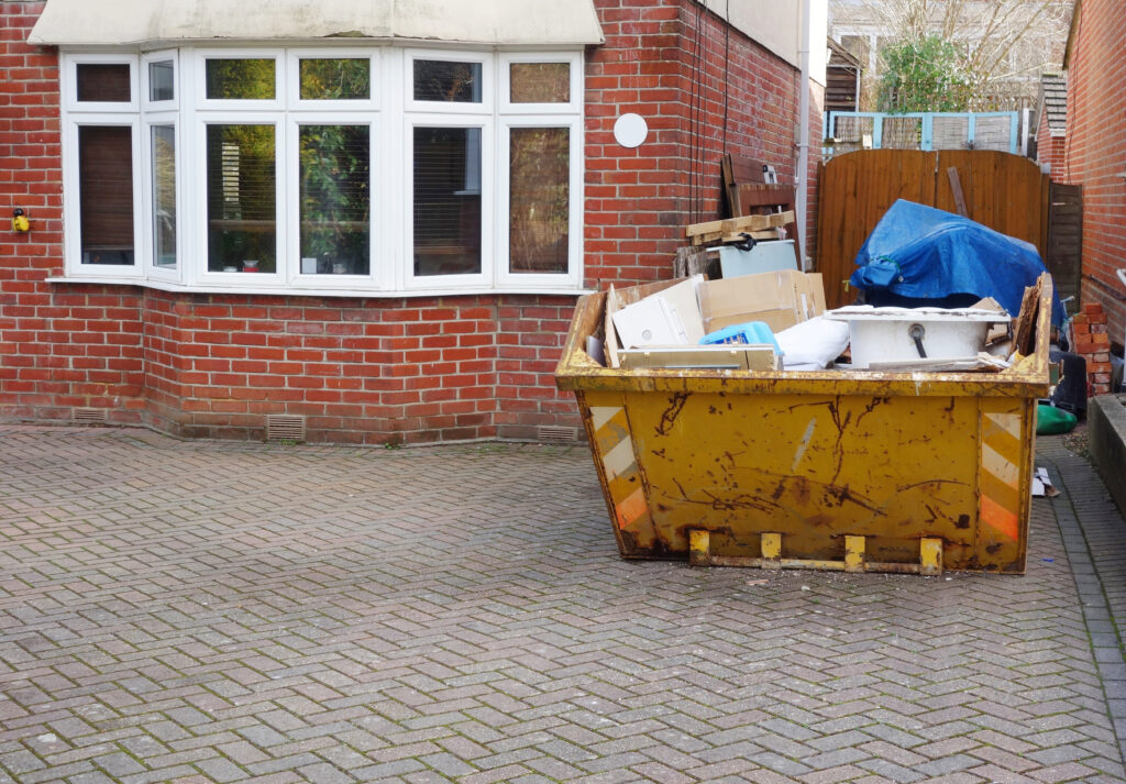 An image of a skip full of rubbish outside someones house, on the driveway.