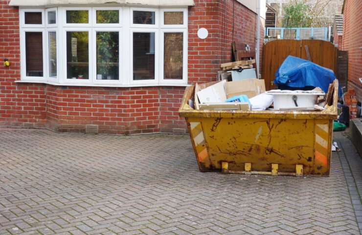An image of a skip full of rubbish outside someones house, on the driveway.
