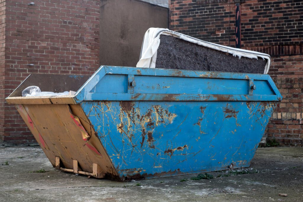 A blue skip with a mattress inside it.