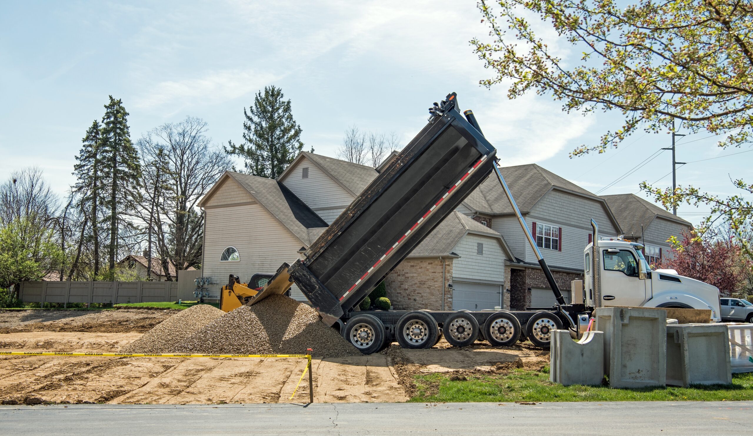 A house with a large truck dropping aggregate out onto the ground.